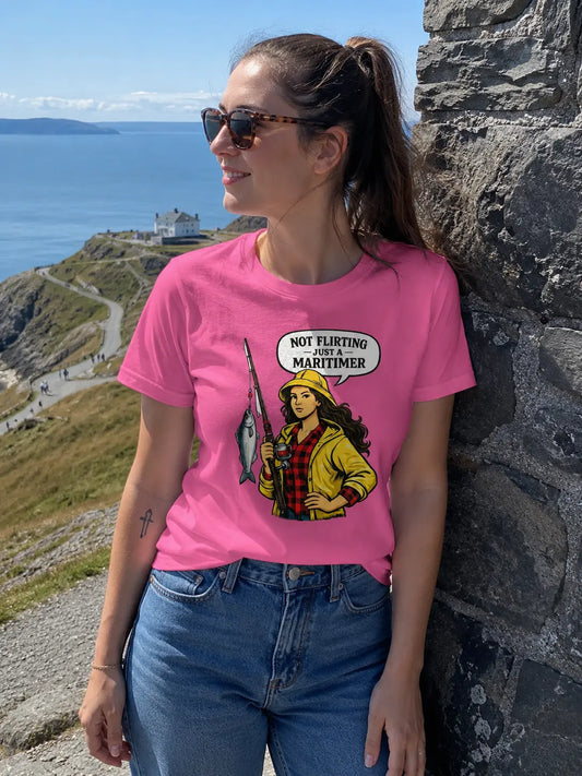Woman wearing a pink t-shirt with a graphic design, standing outdoors near a stone wall with a scenic background.